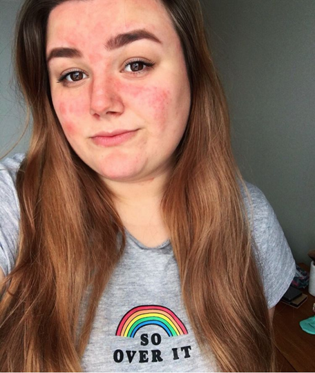 Alice has long brown hair. She gives a reserved smile and wears a gray t-shirt that says "so over it" with a rainbow over it. 