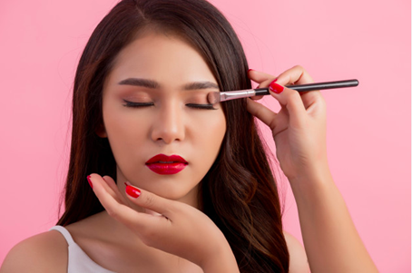 The picture shows a woman who is model-like who is getting glammed up with sparkly eyeshadow.
