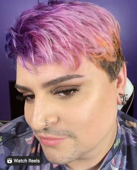 Caleb has short and stylishly cut soft pink, lilac, and purple hair. The colors are distinct but also blend into one another. He glances gently and confidently to the side.