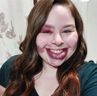 Casey has long brown hair, and she is wearing a emerald green v-neck t-shirt that compliments her hair. She smiles brightly. 