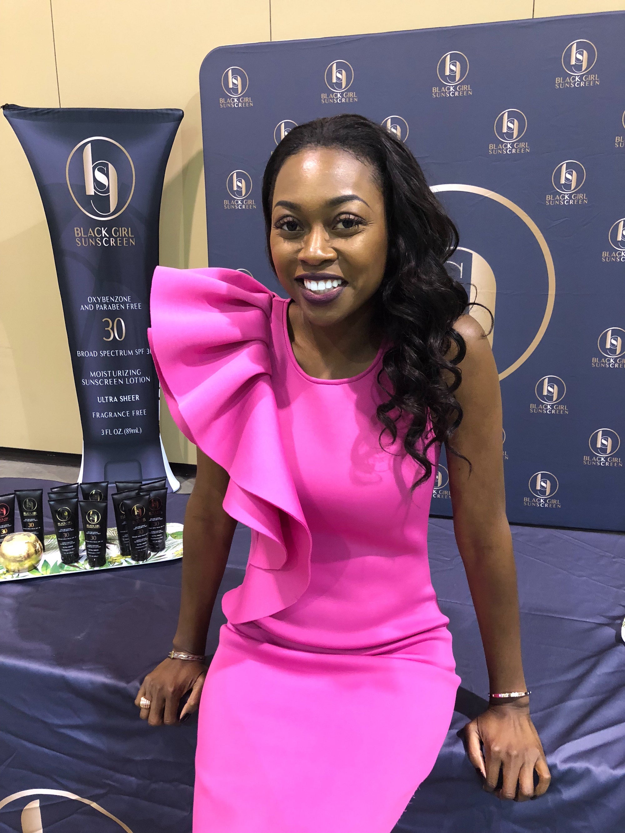Shontay is wearing a flamboyant, hot pink dress. Her hair is thrown to her right shoulder stylishly. She is smiling confidently and gives off a profession air. 
