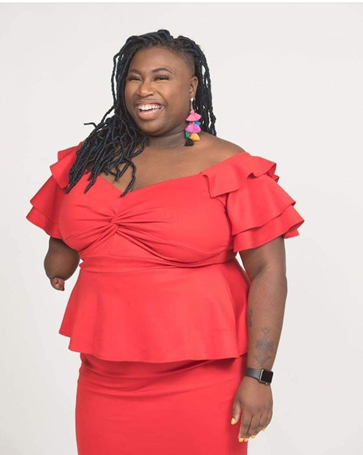 Janessa is an African-American woman who is wearing a bright red blouse and bright red pencil skirt of the same hue to match. She is wearing colorful earrings, and she is wearing dreadlock or thick braids. She smiles gleefully. 