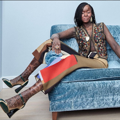 Jeyza has skin composed of many brown hues. She sits cooly on blue sued couch with heels, high fashion slacks, and a very chic vest. She appears self-assured and unintimidated.