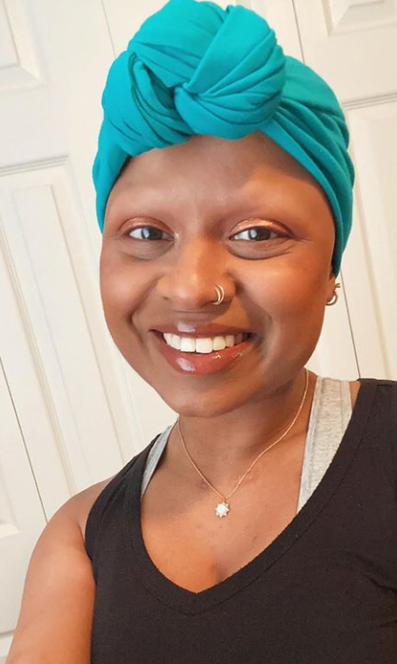 Mohana wears a turquoise head scarf. It is tied into a cute know in the front. She has a nose ring on her right nostril. She has a lighthearted smile.