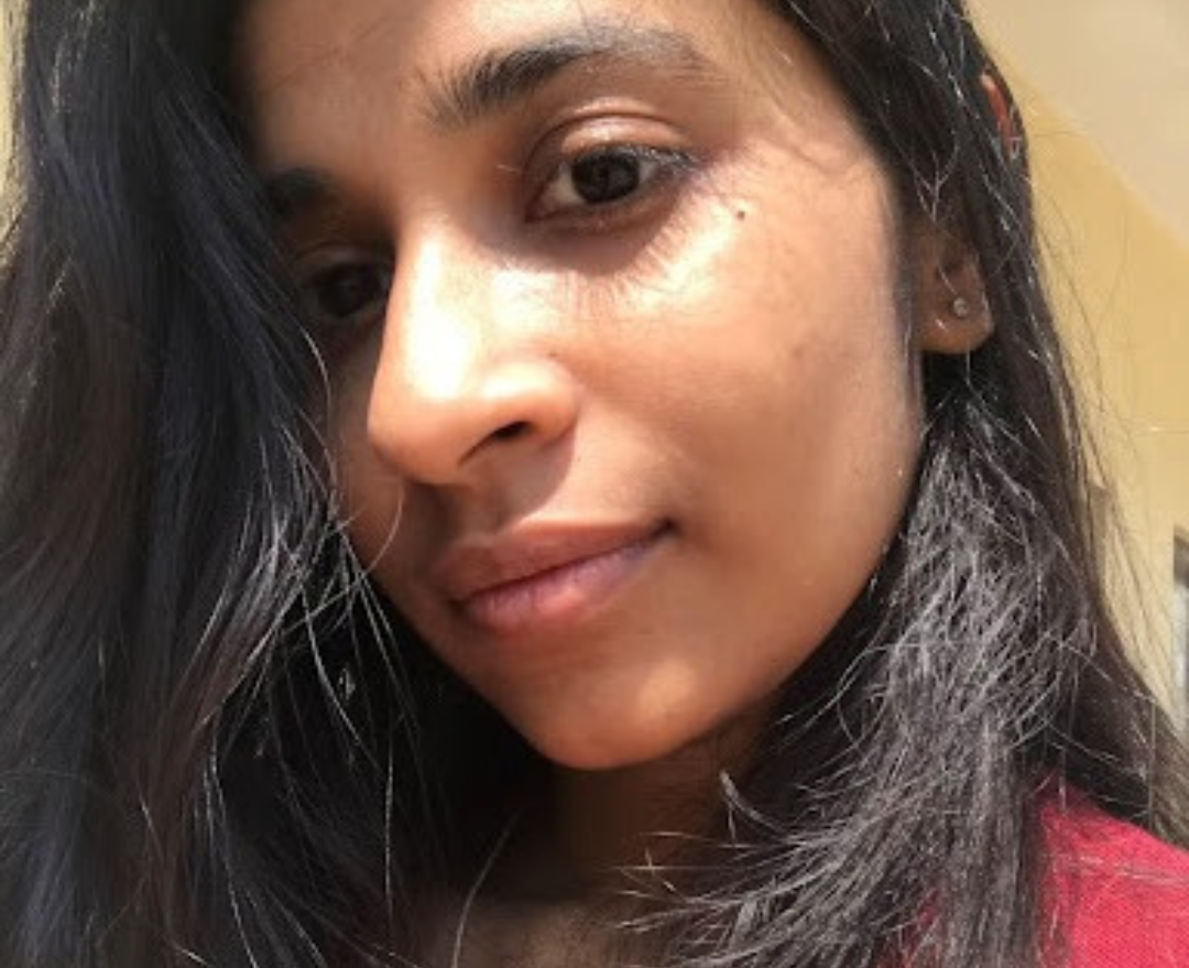 Soumi has light brown skin and chocolate eyes. She is tilting her head to the left, and she is smiling softly. 