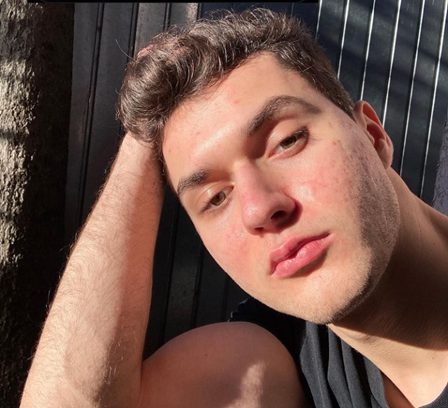 Vlad has thick hair that is cleanly cut high and tight. He has red lips and tan skin. He leans his head into his hand as if he has been having a long conversation with a close friend. 